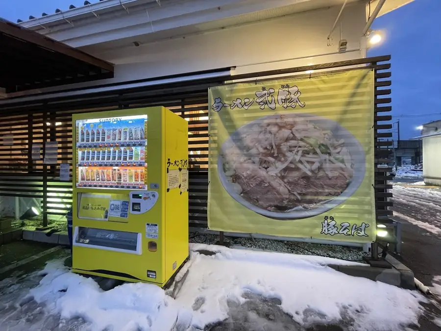 ラーメン弐豚前の黄色い自動販売機と豚そばの描かれた黄色い暖簾