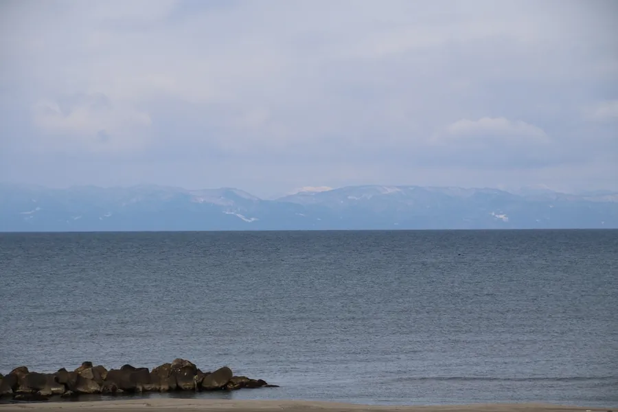 べた凪の日本海と遠くに見える真っ白な金北山